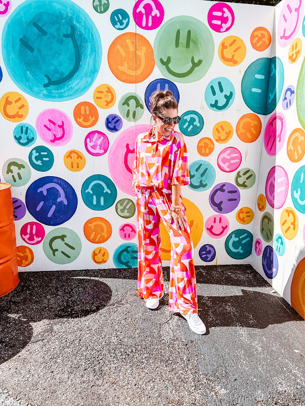 Thin, lightweight and stretchy set featuring fuchsia, orange, coral and ivory abstract print with 1/4 gold button front and collar on the short sleeved top and matching wide leg pants with elastic waist and pockets.