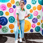 Nearly sheer ivory eyelet patterned blouse with a collar, puff sleeves and three large rhinestone floral buttons at the neckline. The collar, cuffs and hem are a contrasting bright green with pink athletic striping.