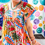 This tropical print short dress features vibrant summer hues with playful striping and fruit motifs throughout, square smocked neckline and flutter sleeves and pockets—complete with pink and blue ball tassels. Crafted from soft, lightweight fabric, it's designed to move with you all day long.