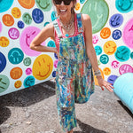 Cotton denim overalls with adjustable straps and sides with metal buttons in a paint splatter detail in cobalt blue, orange, green and yellow washed color with knee darts.
