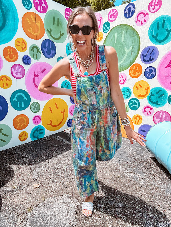 Cotton denim overalls with adjustable straps and sides with metal buttons in a paint splatter detail in cobalt blue, orange, green and yellow washed color with knee darts.