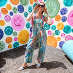 Cotton denim overalls with adjustable straps and sides with metal buttons in a paint splatter detail in cobalt blue, orange, green and yellow washed color with knee darts.