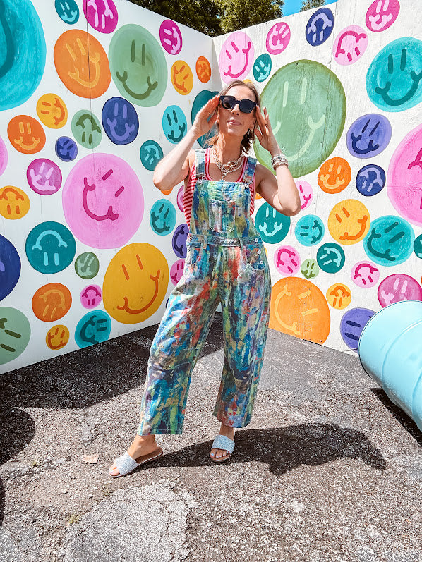 Cotton denim overalls with adjustable straps and sides with metal buttons in a paint splatter detail in cobalt blue, orange, green and yellow washed color with knee darts.