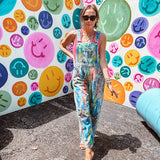 Cotton denim overalls with adjustable straps and sides with metal buttons in a paint splatter detail in cobalt blue, orange, green and yellow washed color with knee darts.