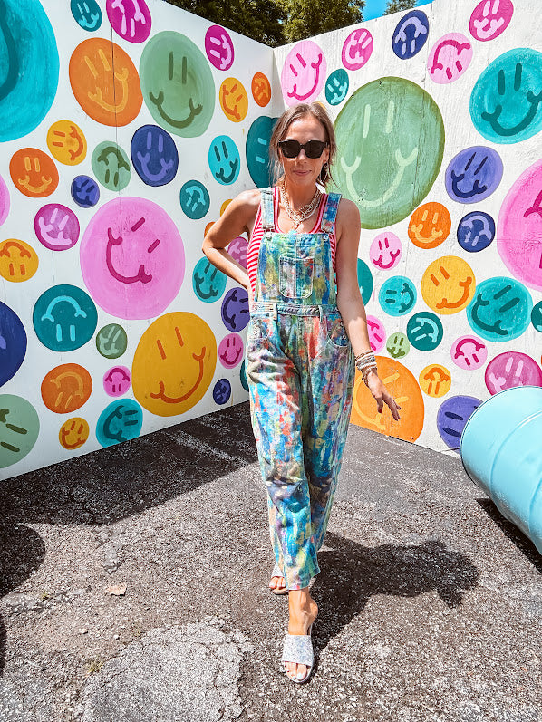 Cotton denim overalls with adjustable straps and sides with metal buttons in a paint splatter detail in cobalt blue, orange, green and yellow washed color with knee darts.