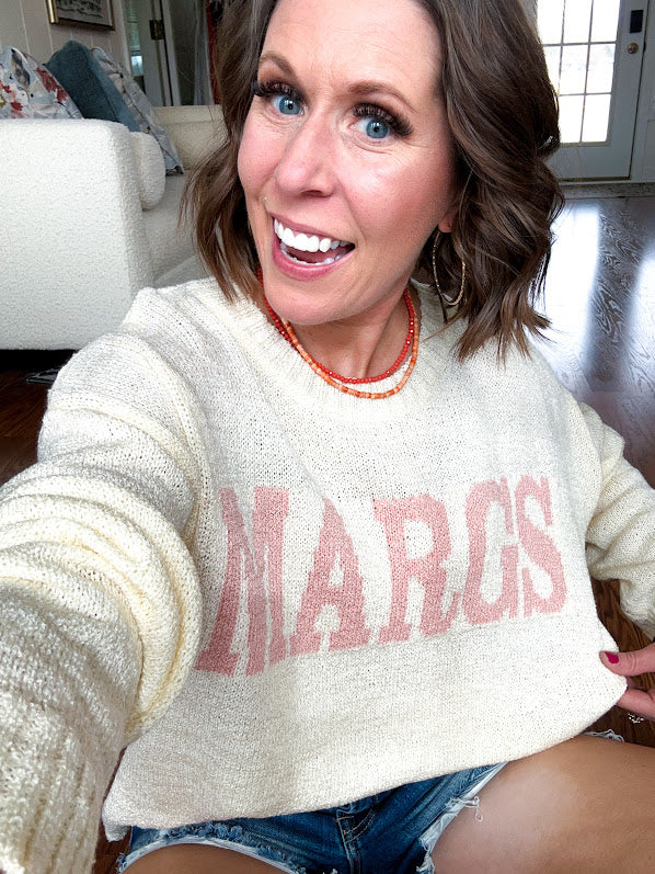 Nearly sheer soft, woven cream sweater with coral "MARGS" on the front.