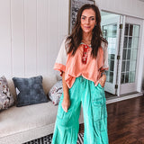 Salmon colored 3/4 sleeve blouse with striped blue and brown yarn collar, three wooden buttons on front, relaxed fit and mesh at the shoulders and sleeves.