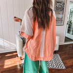 Salmon colored 3/4 sleeve blouse with striped blue and brown yarn collar, three wooden buttons on front, relaxed fit and mesh at the shoulders and sleeves.