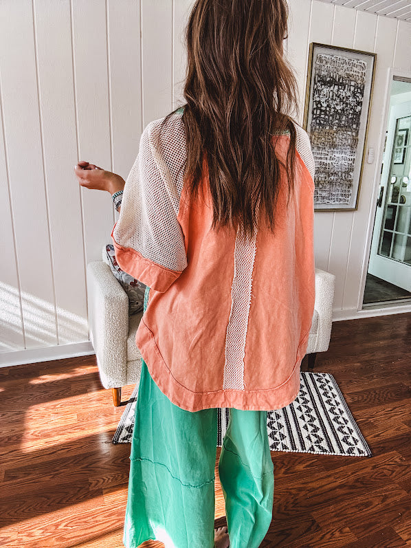 Salmon colored 3/4 sleeve blouse with striped blue and brown yarn collar, three wooden buttons on front, relaxed fit and mesh at the shoulders and sleeves.