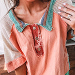 Salmon colored 3/4 sleeve blouse with striped blue and brown yarn collar, three wooden buttons on front, relaxed fit and mesh at the shoulders and sleeves.