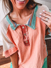 Salmon colored 3/4 sleeve blouse with striped blue and brown yarn collar, three wooden buttons on front, relaxed fit and mesh at the shoulders and sleeves.