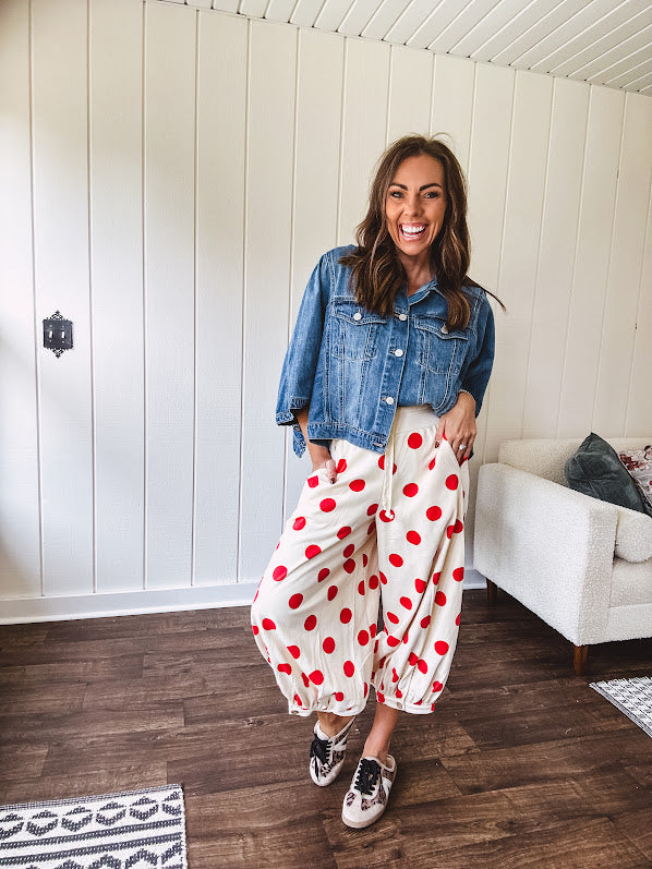 Soft, stretchy cream elastic drawstring waist pants with large red polka dots throughout, pockets and button cuffs for a balloon-like silhouette.
