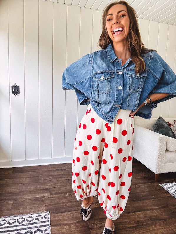 Soft, stretchy cream elastic drawstring waist pants with large red polka dots throughout, pockets and button cuffs for a balloon-like silhouette.