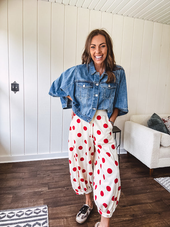 Soft, stretchy cream elastic drawstring waist pants with large red polka dots throughout, pockets and button cuffs for a balloon-like silhouette.