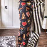 Lightweight denim-like non-stretch wide leg pants with elastic back waist, side and back pockets, button and zipper closure and black and cream stripes on one leg and funky leopard, heart, eye graphics on a black background on the other.