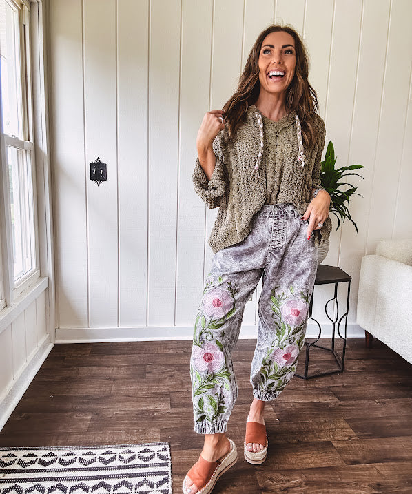 Lightweight washed black joggers with elastic back, floral button down closure and pink and green oversized floral embroidery down the front of both legs.