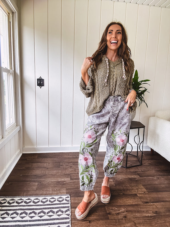 Lightweight washed black joggers with elastic back, floral button down closure and pink and green oversized floral embroidery down the front of both legs.