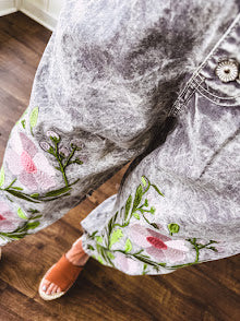 Lightweight washed black joggers with elastic back, floral button down closure and pink and green oversized floral embroidery down the front of both legs.