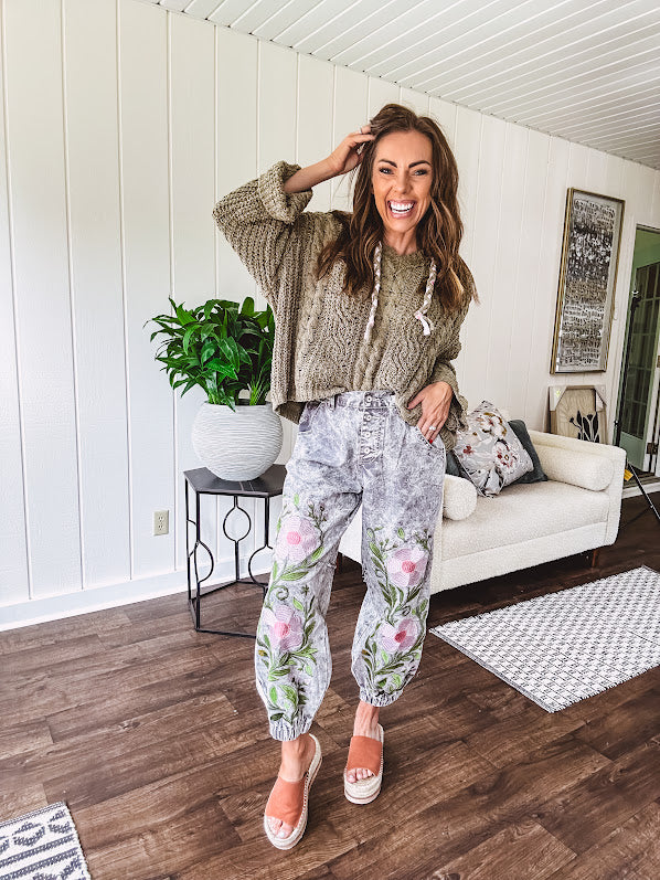 Lightweight washed black joggers with elastic back, floral button down closure and pink and green oversized floral embroidery down the front of both legs.