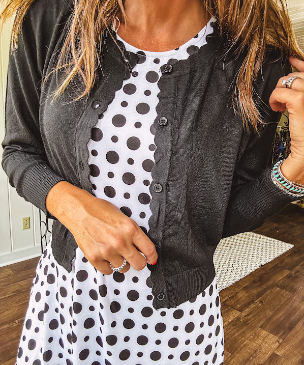 Lightweight, long sleeved black cardigan with button front and scalloped trim with cropped hem.