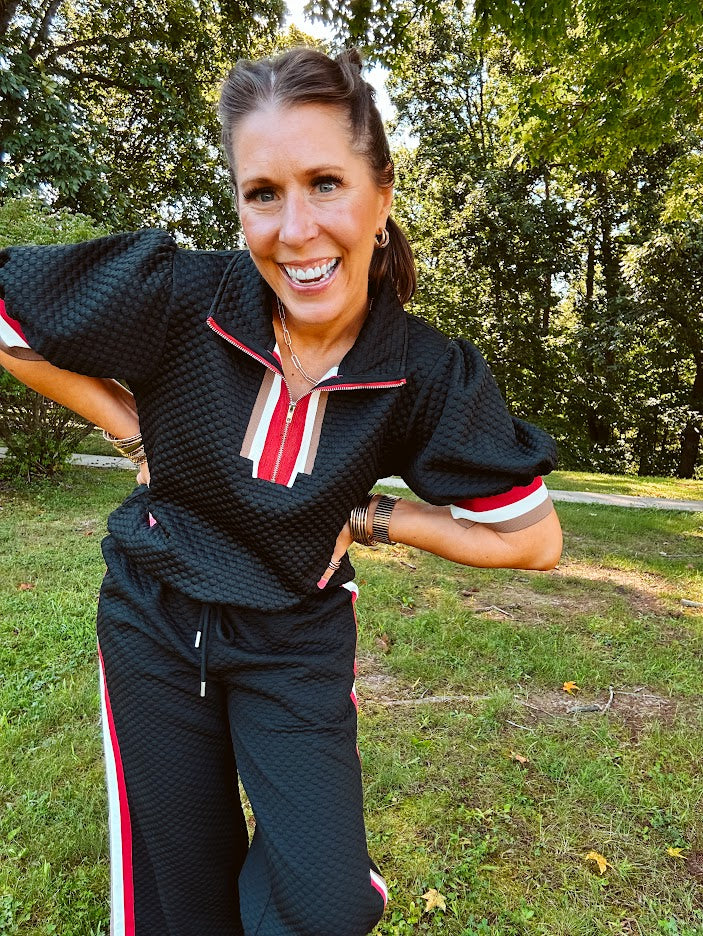 Black quilted top with cream, red and taupe stripes along the 1/4 zip neckline and cuffs with puff sleeves.