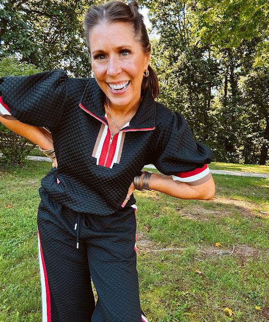 Black quilted short sleeved top with puff sleeves, 1/4 zip and taupe, red and cream striping detail at the neck and cuffs.