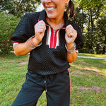 Black quilted short sleeved top with puff sleeves, 1/4 zip and taupe, red and cream striping detail at the neck and cuffs.