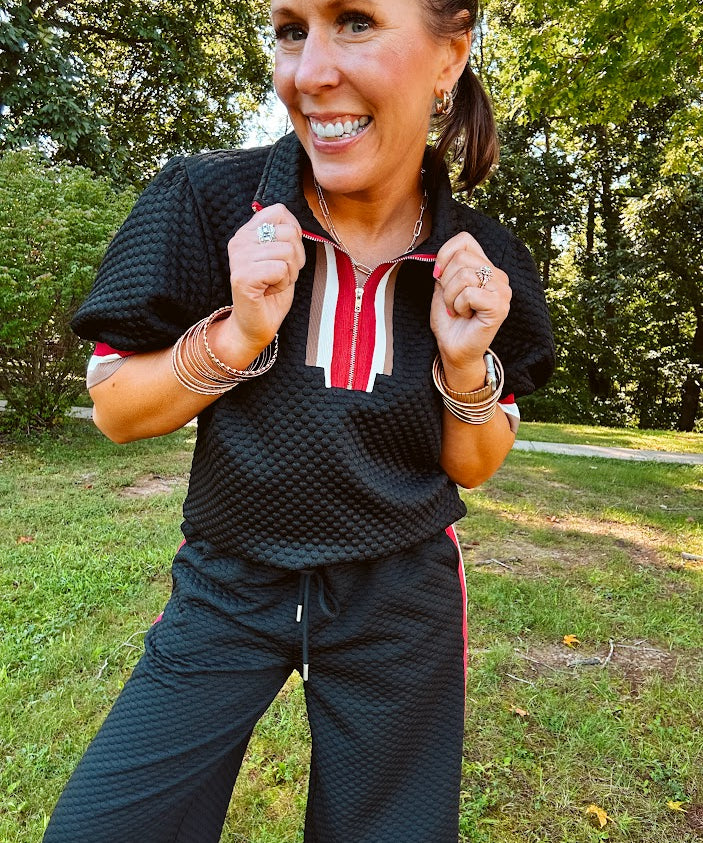 Black quilted top with cream, red and taupe stripes along the 1/4 zip neckline and cuffs with puff sleeves.
