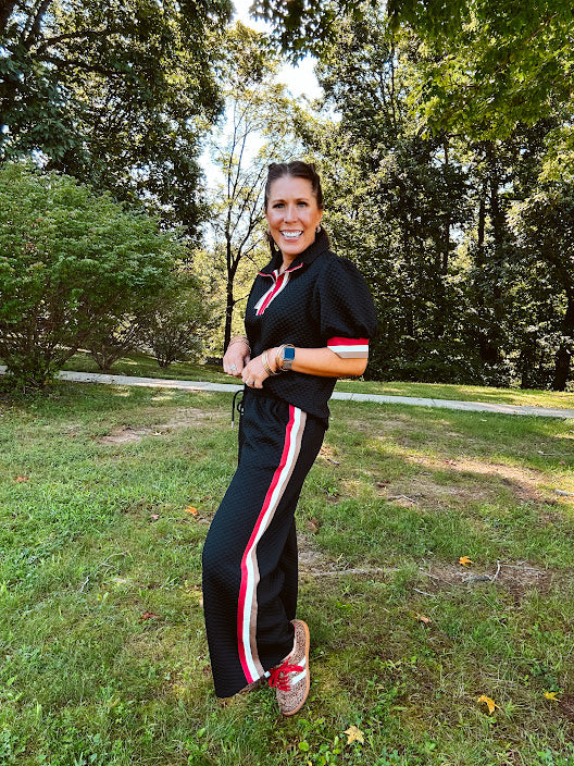 Black quilted short sleeved top with puff sleeves, 1/4 zip and taupe, red and cream striping detail at the neck and cuffs.