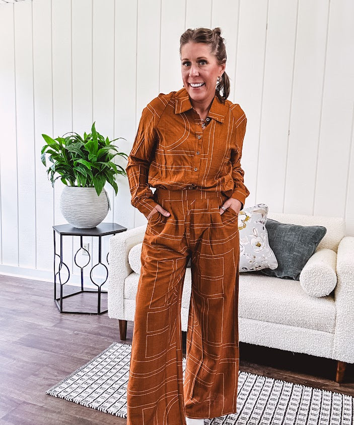 Wide leg rust pants with elastic waist and front pleats with geometric white stitching print throughout.