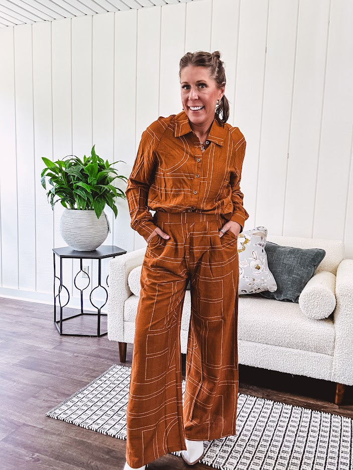 Wide leg rust pants with elastic waist and front pleats with geometric white stitching print throughout.