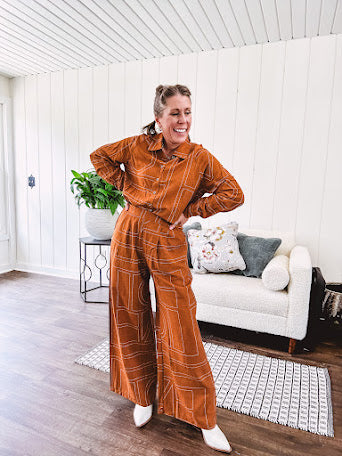 Wide leg rust pants with elastic waist and front pleats with geometric white stitching print throughout.