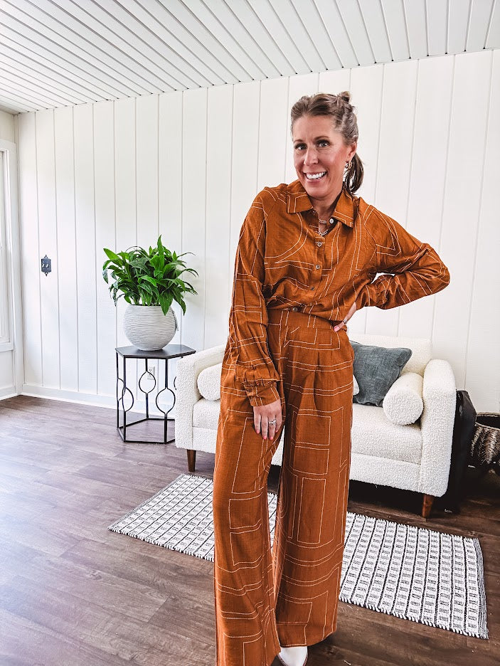Wide leg rust pants with elastic waist and front pleats with geometric white stitching print throughout.