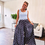 Thin, lightweight ultra wide leg pants in dark denim shade with light blue polka dots throughout and elastic waist with ruffles on the waist and front pockets.
