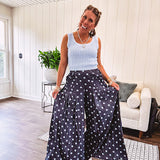 Thin, lightweight ultra wide leg pants in dark denim shade with light blue polka dots throughout and elastic waist with ruffles on the waist and front pockets.