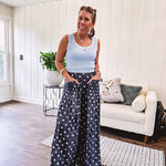 Thin, lightweight ultra wide leg pants in dark denim shade with light blue polka dots throughout and elastic waist with ruffles on the waist and front pockets.