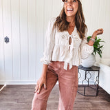 Lightweight long sleeved top in light khaki with two front bow ties at the deep scalloped V neck, eyelet embroidered flowers on the front and ruffled hem at the waist.