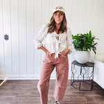 Lightweight long sleeved top in light khaki with two front bow ties at the deep scalloped V neck, eyelet embroidered flowers on the front and ruffled hem at the waist.