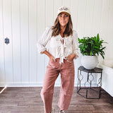 Lightweight long sleeved top in light khaki with two front bow ties at the deep scalloped V neck, eyelet embroidered flowers on the front and ruffled hem at the waist.