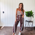 Dark brown slick track pants with white stripe detail down the sides and on the cutout hem with drawstring elastic waist and side pockets.