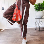Dark brown slick track pants with white stripe detail down the sides and on the cutout hem with drawstring elastic waist and side pockets.