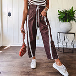 Dark brown slick track pants with white stripe detail down the sides and on the cutout hem with drawstring elastic waist and side pockets.