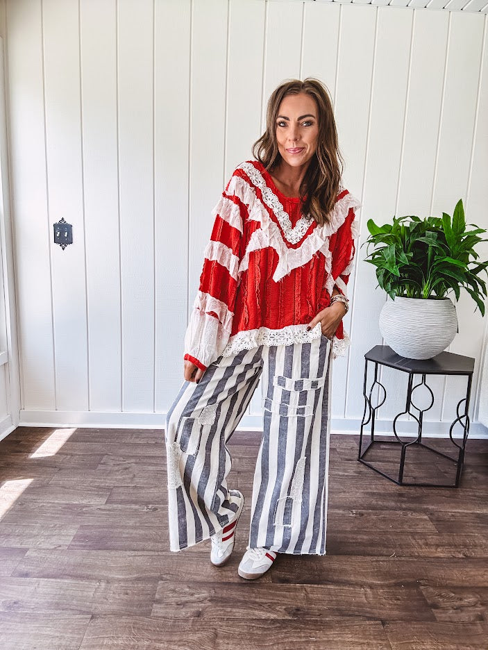 Apple red ruffle texture boho style long sleeved top with round neck and cream eyelet lace detail in a V shape across the front and on the sleeves and hem.