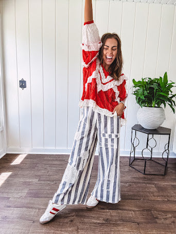 Apple red ruffle texture boho style long sleeved top with round neck and cream eyelet lace detail in a V shape across the front and on the sleeves and hem.