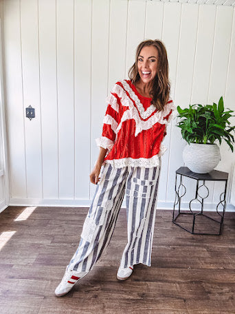 Apple red ruffle texture boho style long sleeved top with round neck and cream eyelet lace detail in a V shape across the front and on the sleeves and hem.