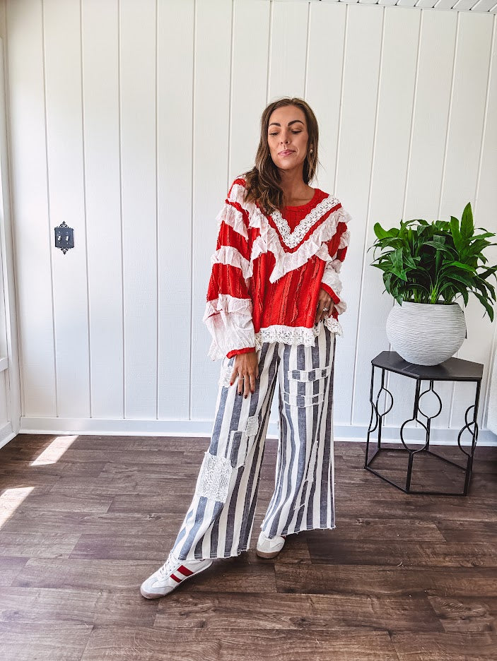Apple red ruffle texture boho style long sleeved top with round neck and cream eyelet lace detail in a V shape across the front and on the sleeves and hem.
