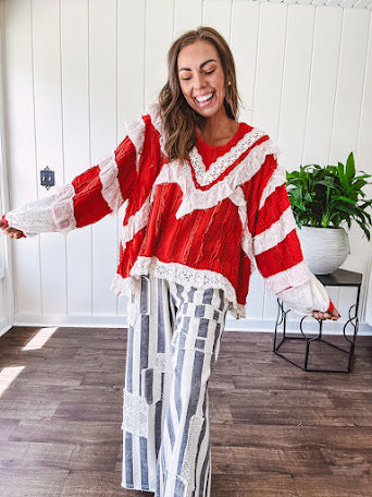 Apple red ruffle texture boho style long sleeved top with round neck and cream eyelet lace detail in a V shape across the front and on the sleeves and hem.
