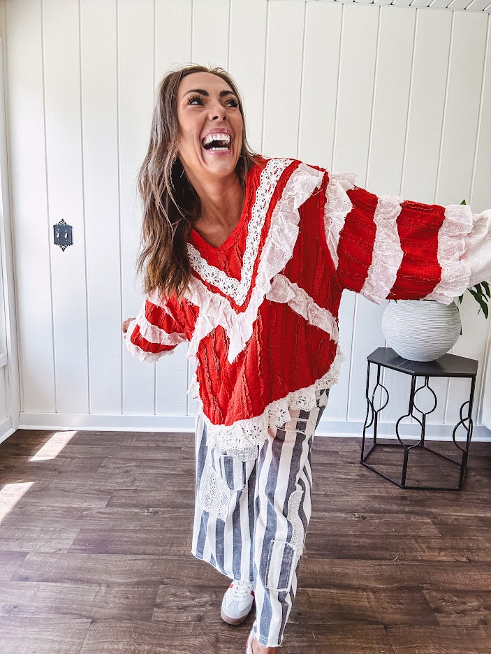 Apple red ruffle texture boho style long sleeved top with round neck and cream eyelet lace detail in a V shape across the front and on the sleeves and hem.