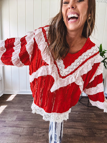 Apple red ruffle texture boho style long sleeved top with round neck and cream eyelet lace detail in a V shape across the front and on the sleeves and hem.
