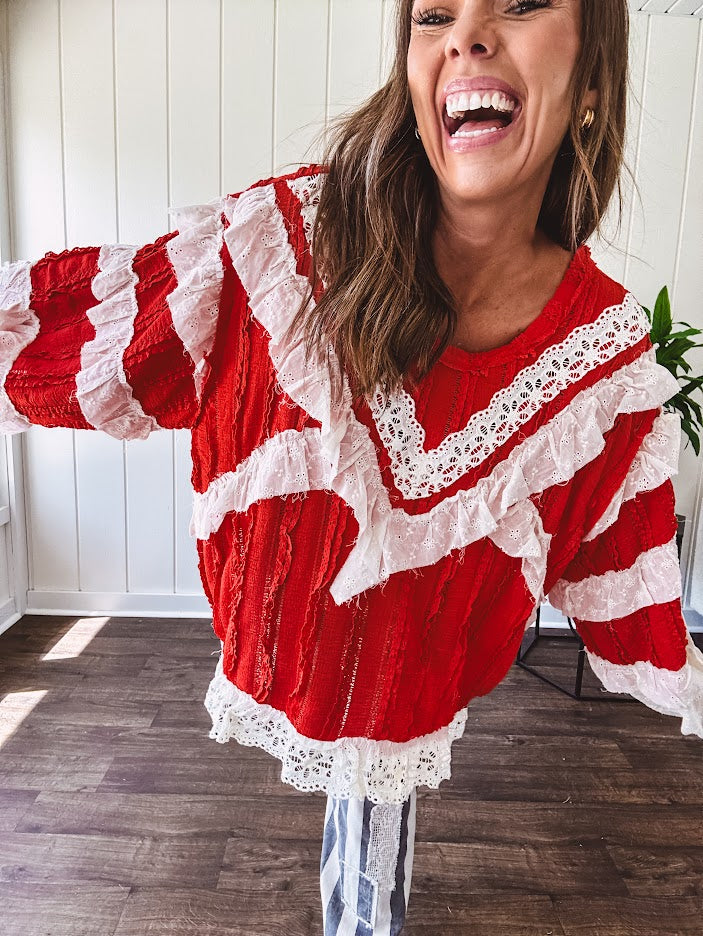 Apple red ruffle texture boho style long sleeved top with round neck and cream eyelet lace detail in a V shape across the front and on the sleeves and hem.